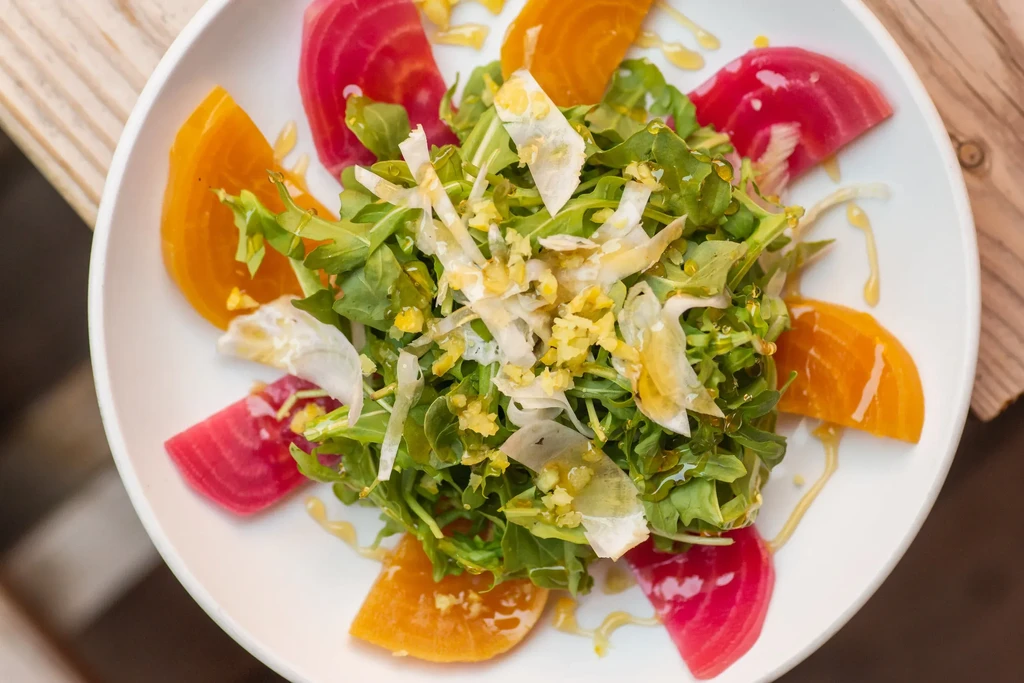 Vibrant arugula salad with shaved cheese, beet slices, and dressing.
