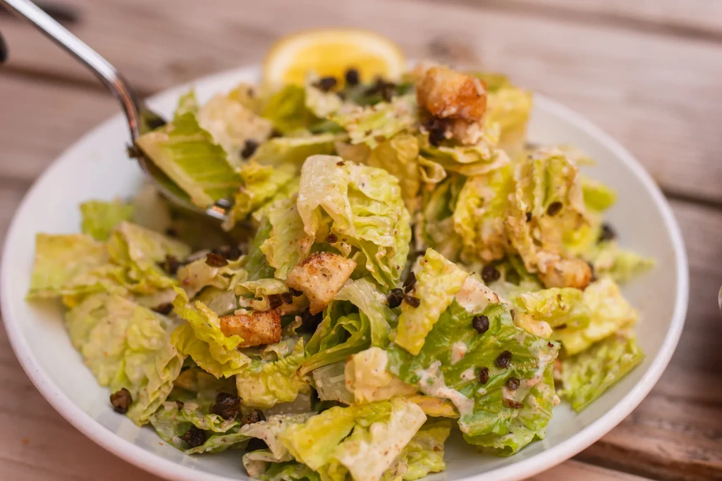 Caesar salad with croutons and a fork in a white bowl.