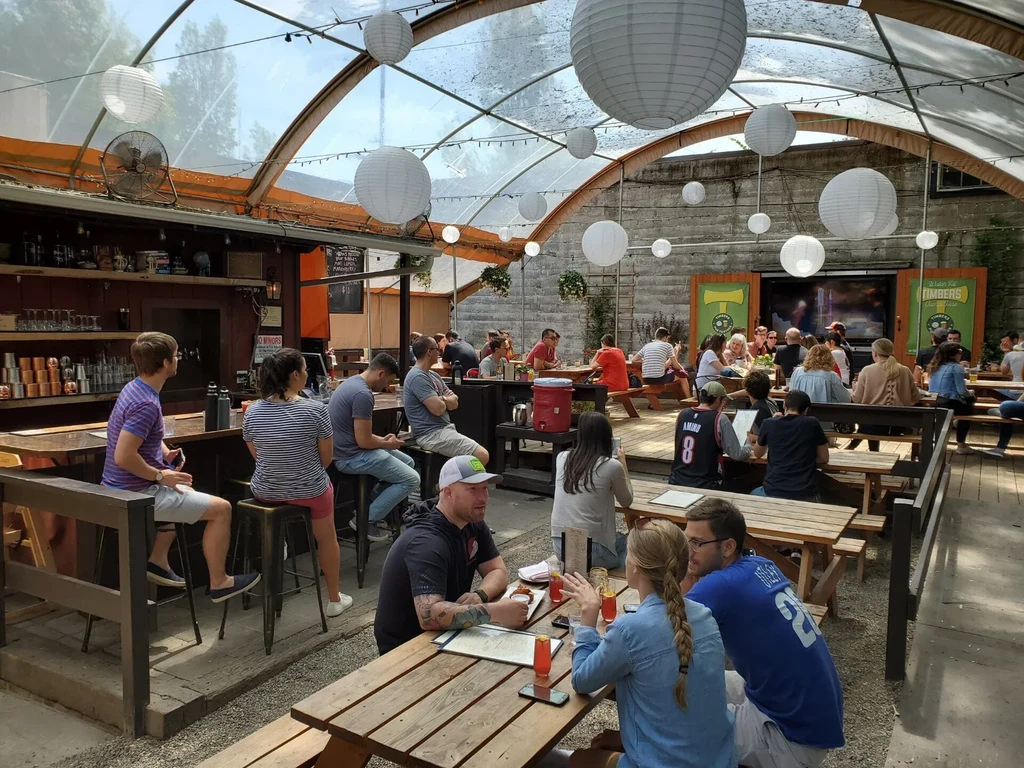 Bustling outdoor patio under arched roof with lanterns and people dining.