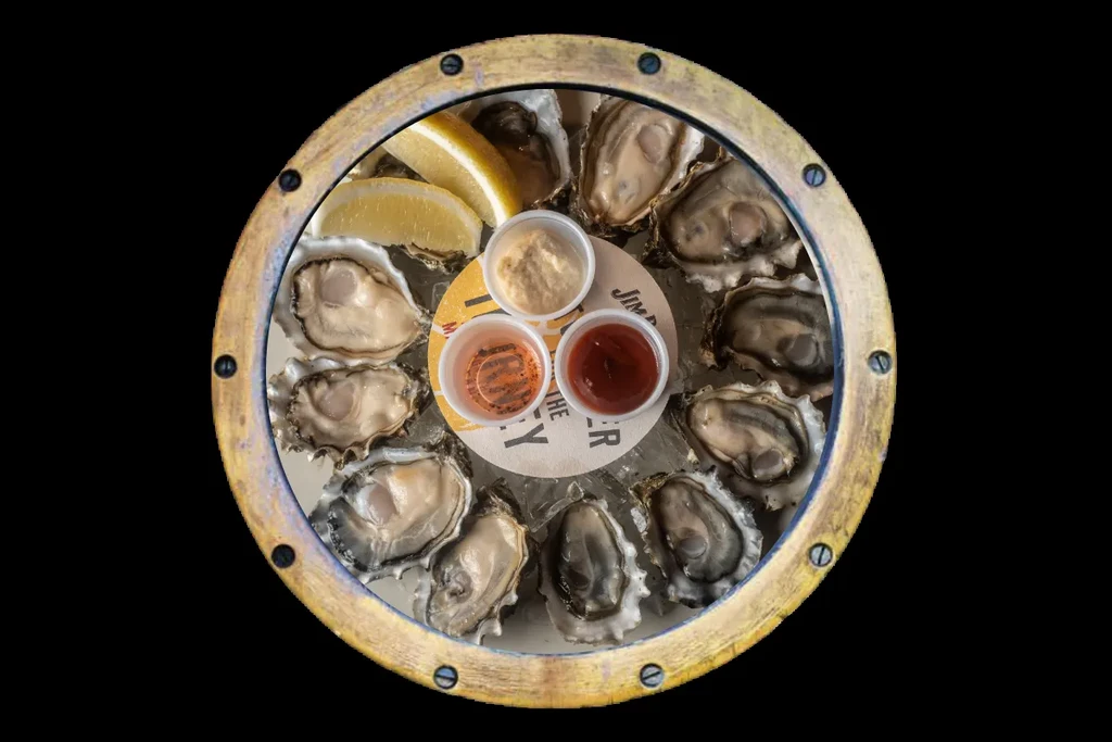 Fresh oysters, lemon, and sauces on ice in a rustic tray.