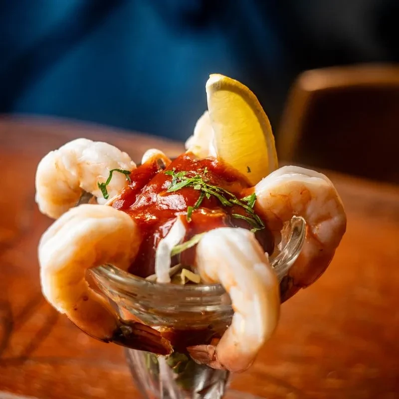 Shrimp cocktail in a glass, topped with sauce, lemon, and herbs.