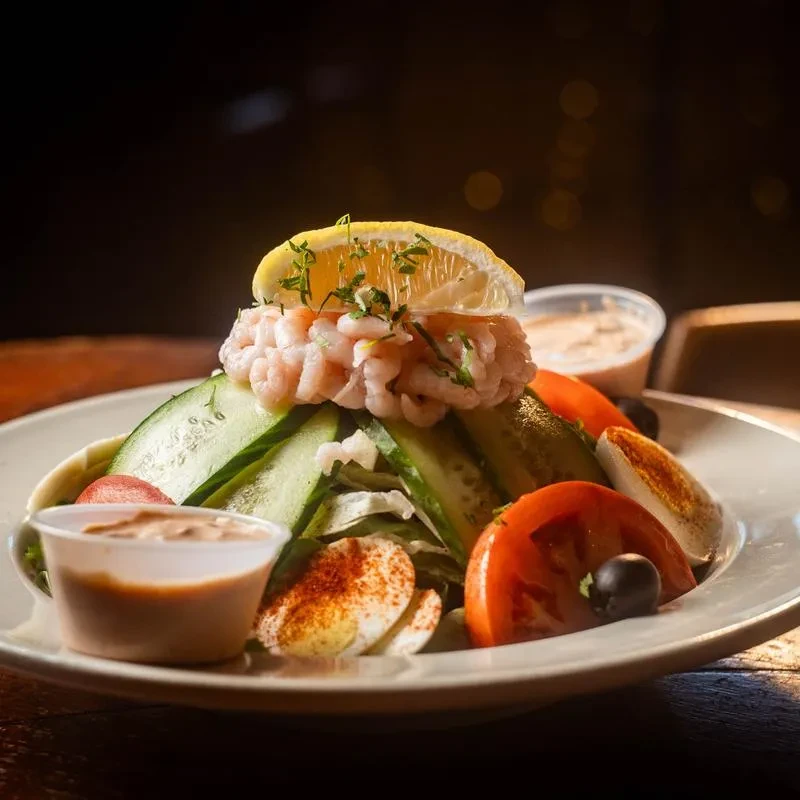 Large shrimp salad with lemon, hard-boiled eggs, tomatoes, and olives.