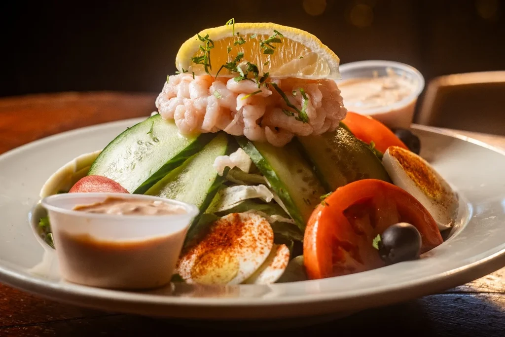 Shrimp salad with lemon, eggs, cucumber, tomatoes, olives, and dressing.