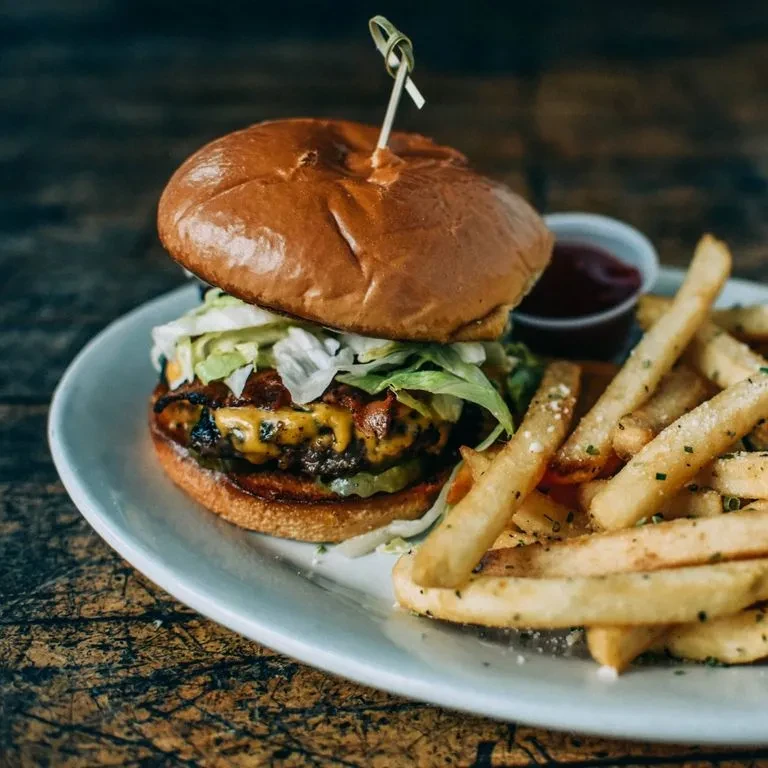 Burger with melted cheese, bacon, seasoned fries, and ketchup.