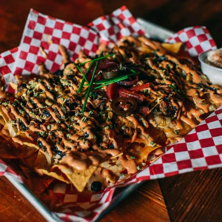 Loaded nachos in a tray with melted cheese, dark toppings, and jalapeños.