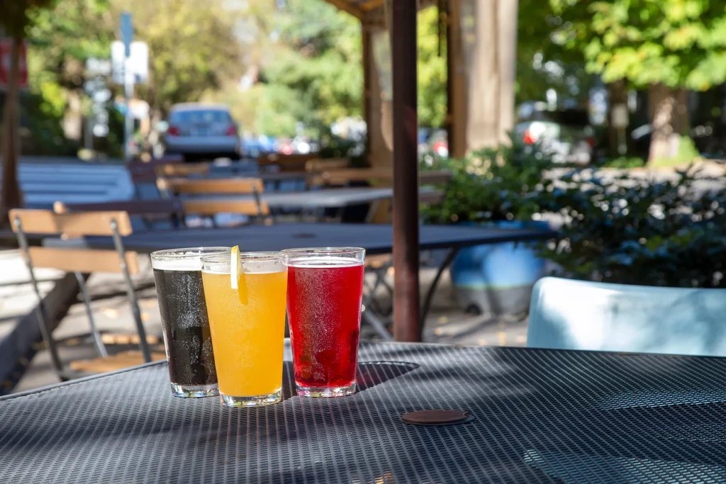 Outdoor table with three sunlit glasses of dark, yellow, and red drinks.