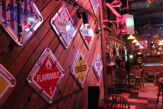 Dimly lit bar interior with wooden wall displaying hazard signs.