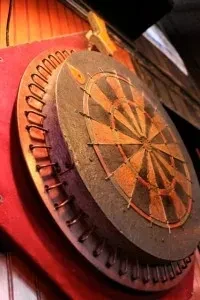 Close-up of an antique-style dartboard with a red frame on a wooden wall.