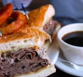 Roast beef sandwich cut in half with onion rings and coffee.