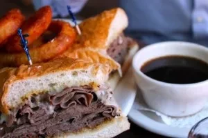 Roast beef sandwich, onion rings, and coffee served on a plate.