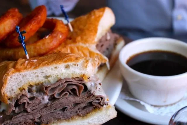 Close-up of French dip sandwich, onion rings, and au jus.