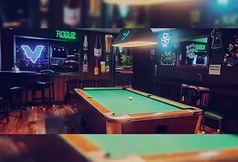 Moody, dimly lit bar with a pool table and neon signs.