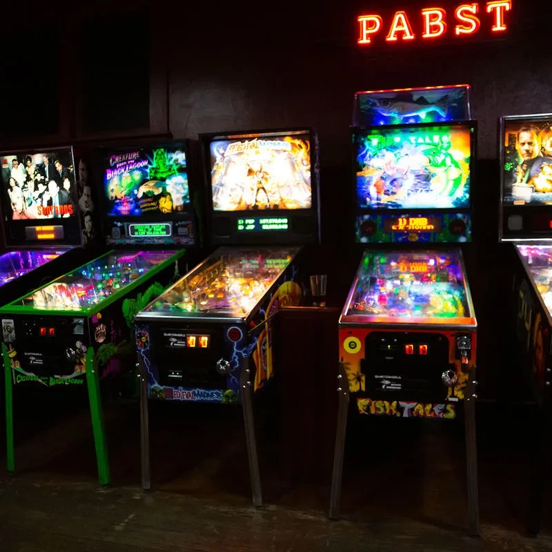 Brightly lit pinball machines in a dark arcade under a red PABST sign.