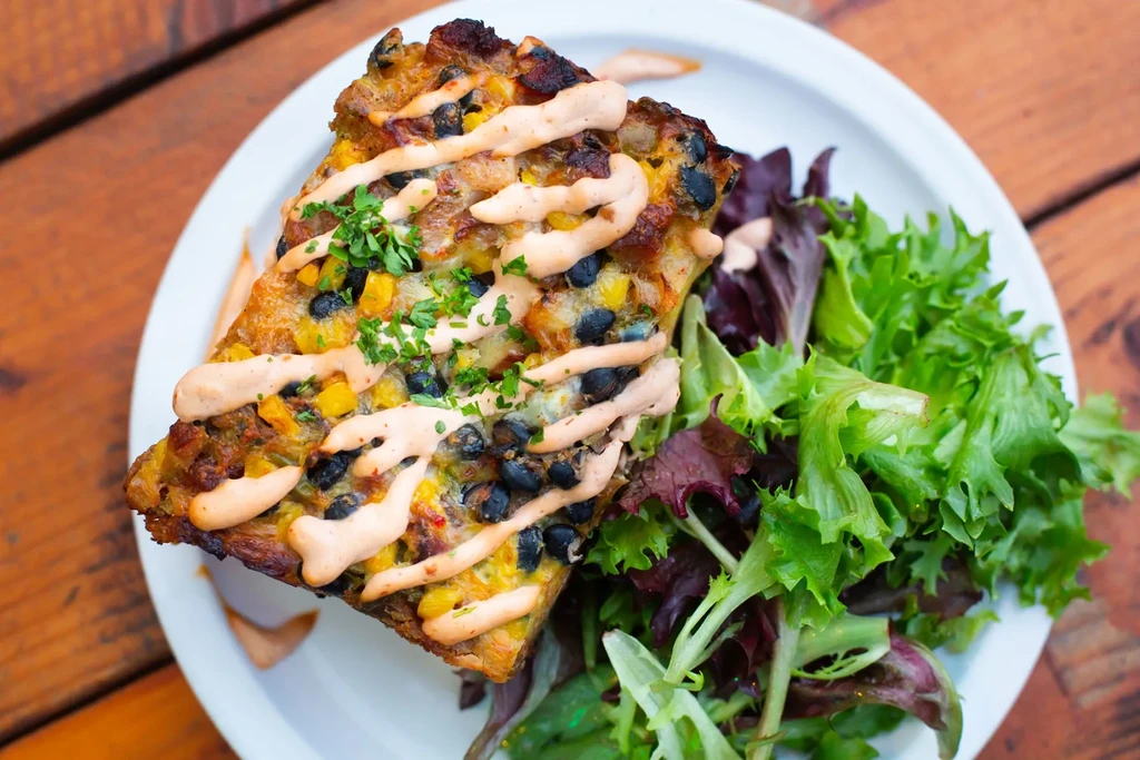 Baked dish with corn, black beans, cheese, sauce, herbs, and salad.