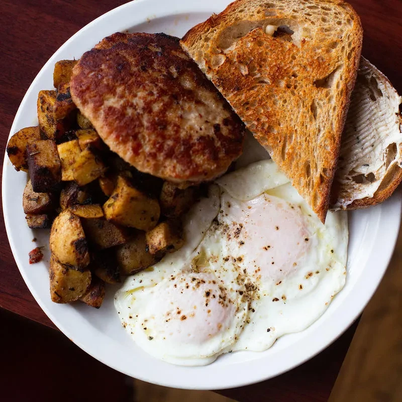Overhead: hearty breakfast with sausage, sunny-side eggs, home fries, toast.