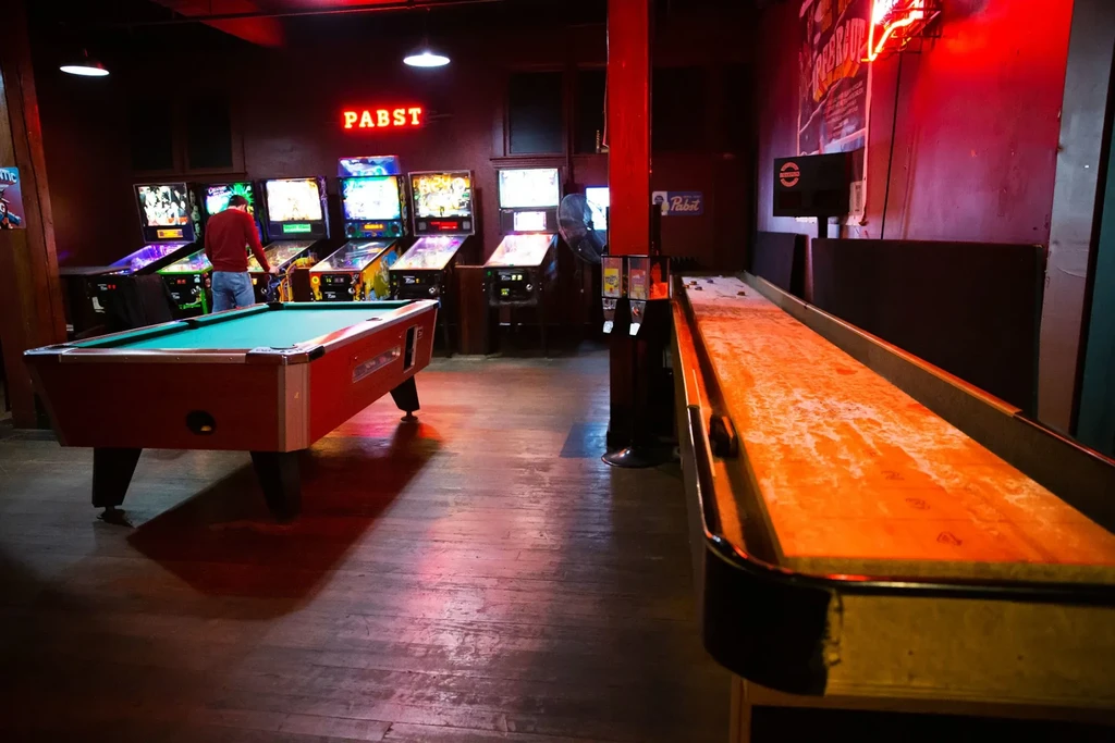 Pool table, shuffleboard, and pinball machines in a dimly lit bar.