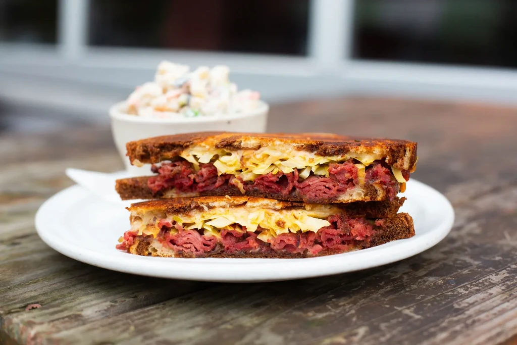 Close-up of a sliced Reuben sandwich on a white plate and wood.