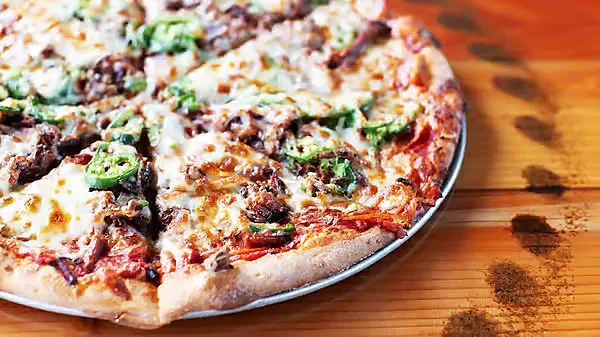 Close-up of pizza topped with jalapenos and steak on wood table