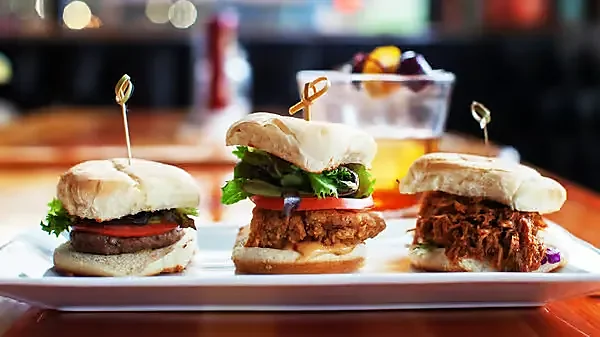 Three sliders on white plate with beer and side salad