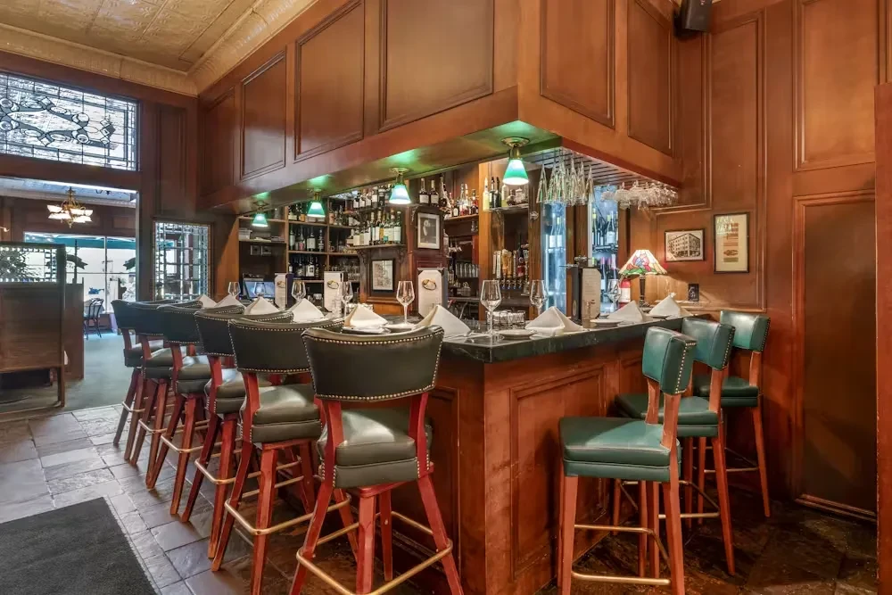 Ornate dark wood bar, leather stools with place settings, and liquor bottles.