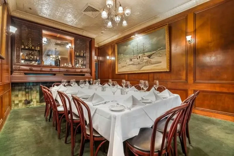 Formal dining room: set table, dark wood paneling, bar, ship painting.