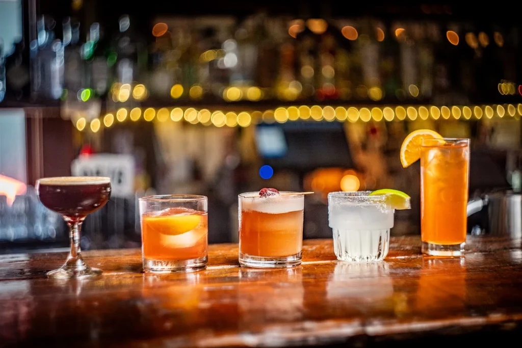 Five distinct cocktails lined up on a polished wooden bar.