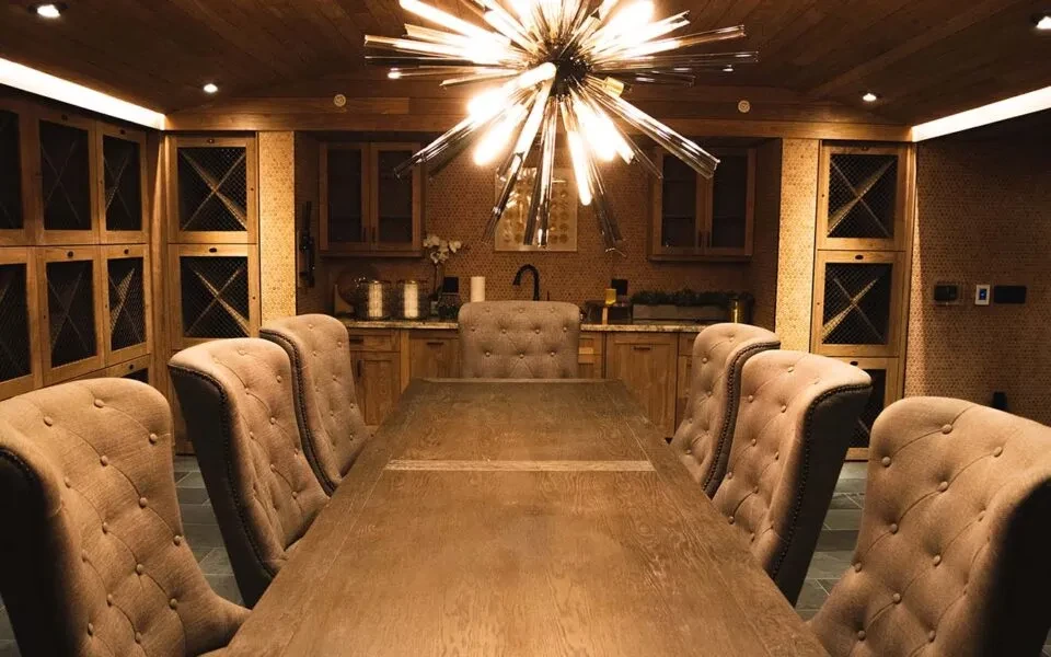 Private dining room with long wooden table, plush chairs, modern chandelier.