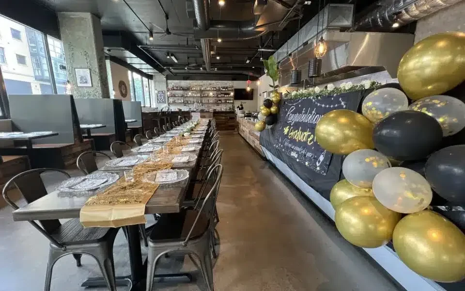 Modern restaurant with graduation decor, long table, bar, and city views.