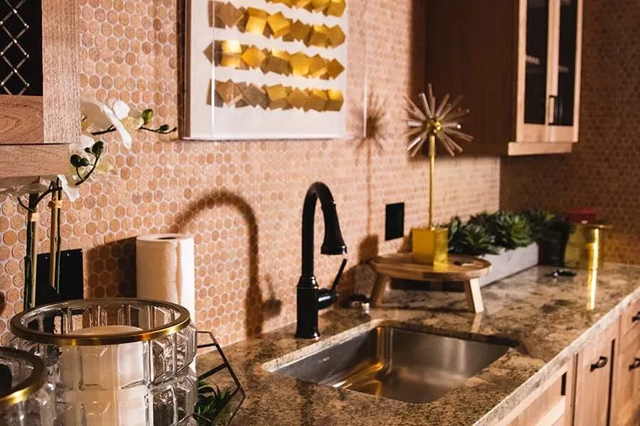 Modern kitchen counter with mosaic backsplash, black faucet, and golden decor.