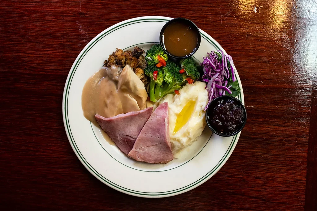Plated roast dinner: ham, chicken, mashed potatoes, vegetables, and sauces.