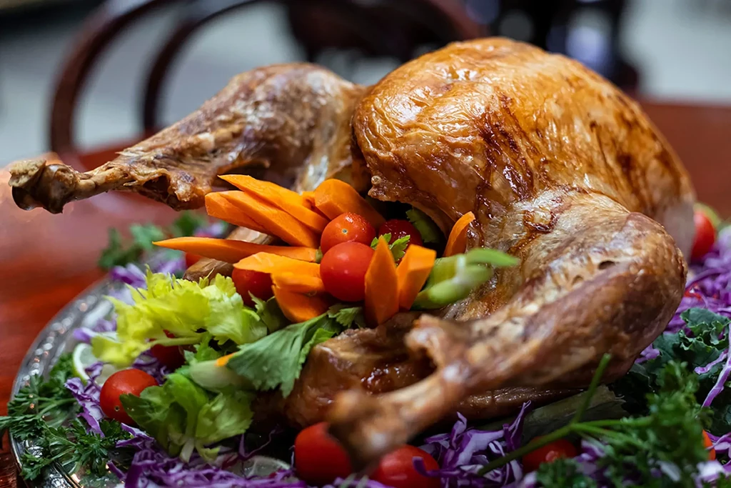 Roasted golden-brown turkey on ornate silver platter with colorful garnishes.