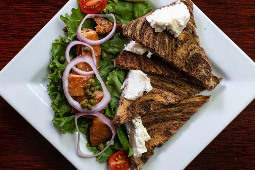 Overhead view: Plated smoked salmon salad and cheese-topped marbled toast.