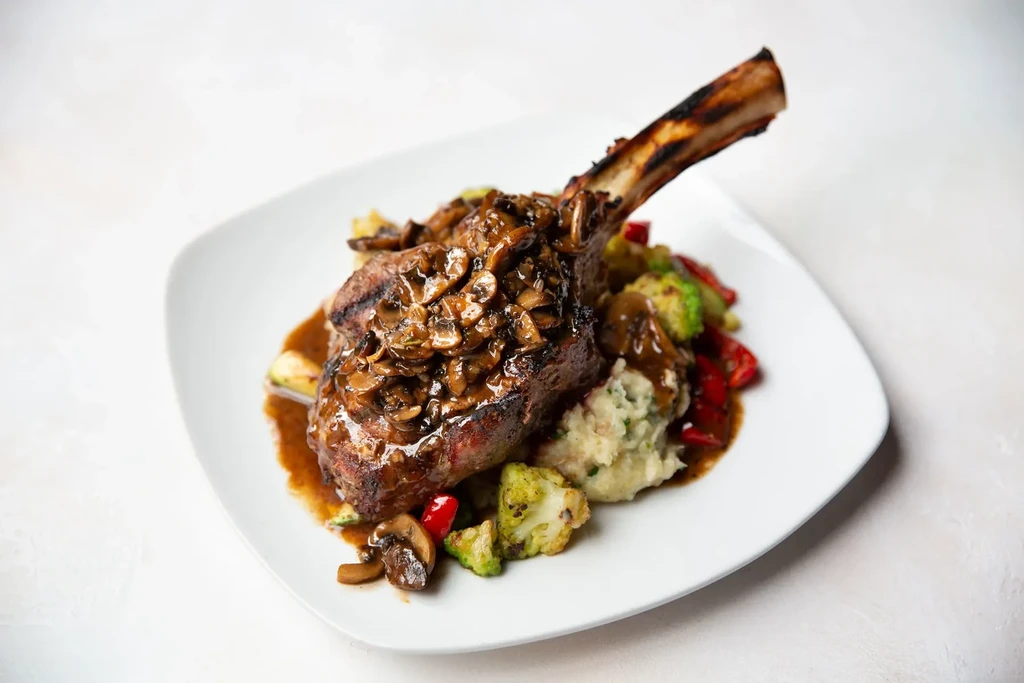 Tomahawk steak with mushroom sauce, mashed potatoes, and roasted vegetables.