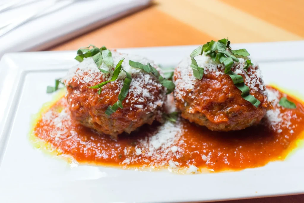 Meatballs topped with cheese and basil in red tomato sauce.