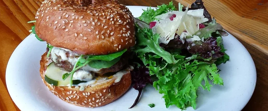 Gourmet burger with creamy sauce and a fresh side salad.