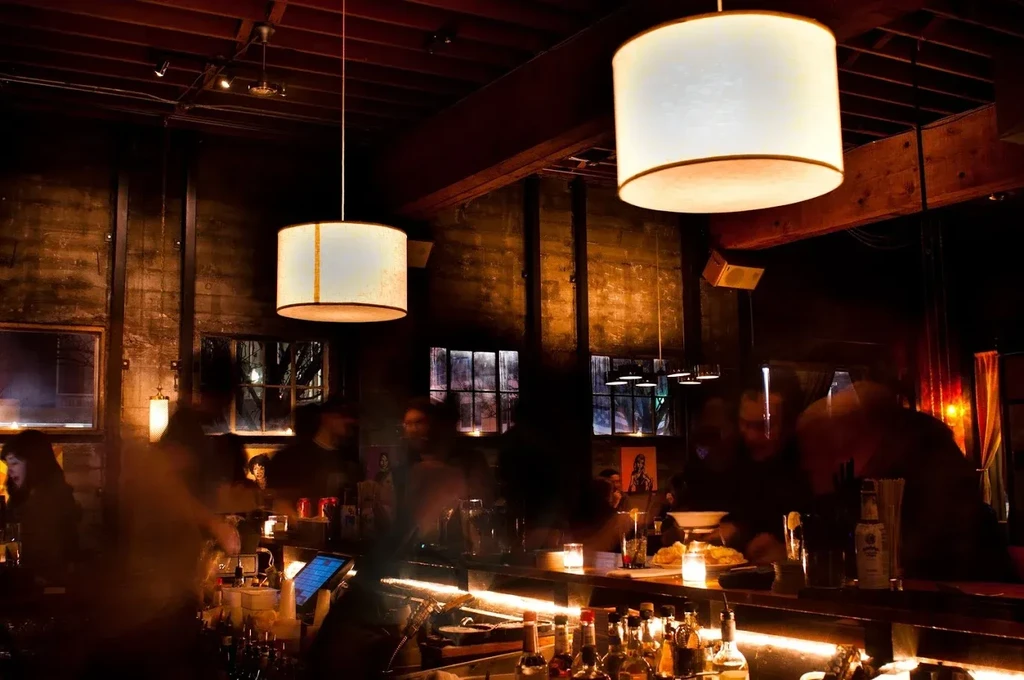 Dimly lit bar interior with blurred people, bottles, and warm pendant lights.