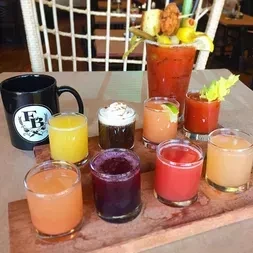 Heavily garnished Bloody Mary, eight colorful drinks, wooden board.