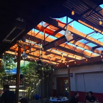 Restaurant patio with wooden ceiling, corrugated panels, string lights, and patrons.