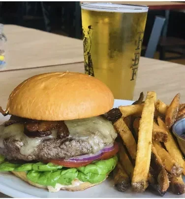 A gourmet burger topped with bacon and cheese, served with fries and beer.