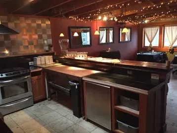 Warm bar interior with wooden counter, open kitchen, and string lights.