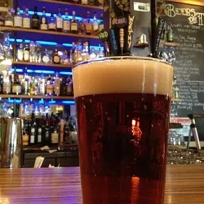 Close-up of amber beer with thick foam on a wooden bar.