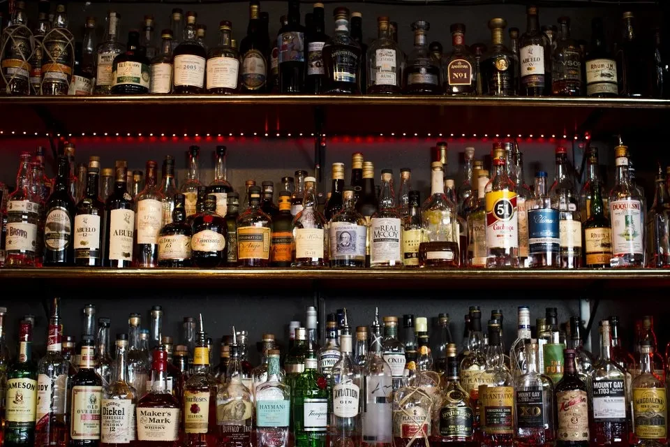 Variety of liquor bottles on metal bar shelves with red LED lighting.