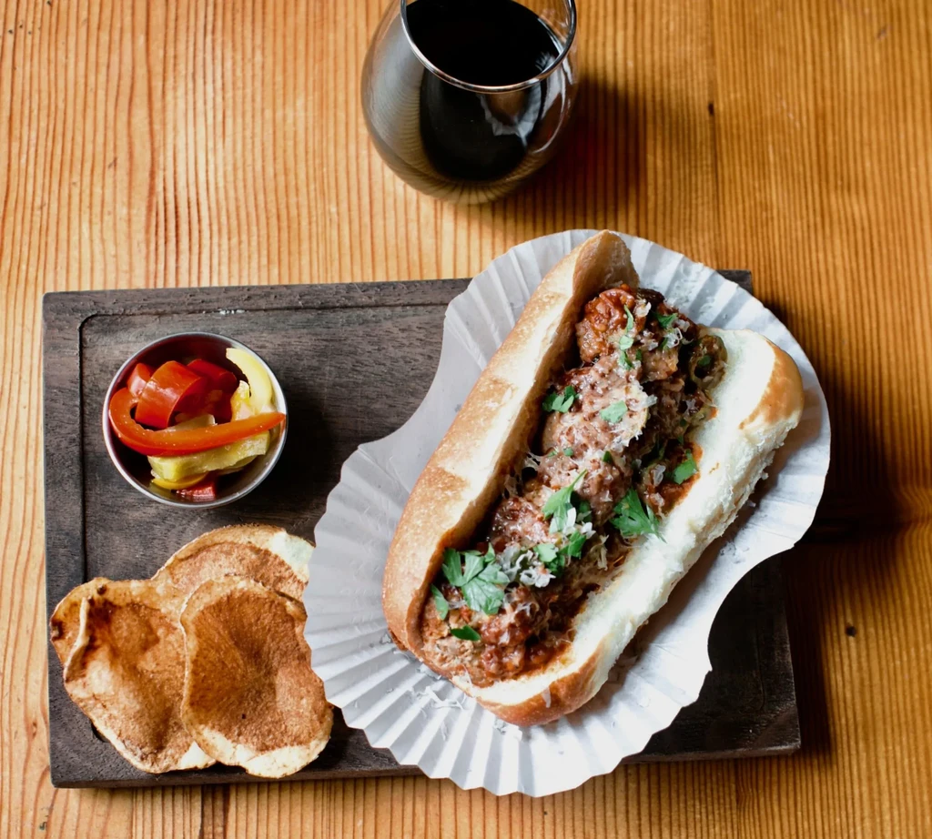 Overhead shot of a meatball sub, pickled vegetables, chips, red wine.