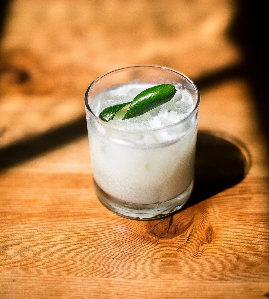 Milky drink with ice and a lime twist on wood.