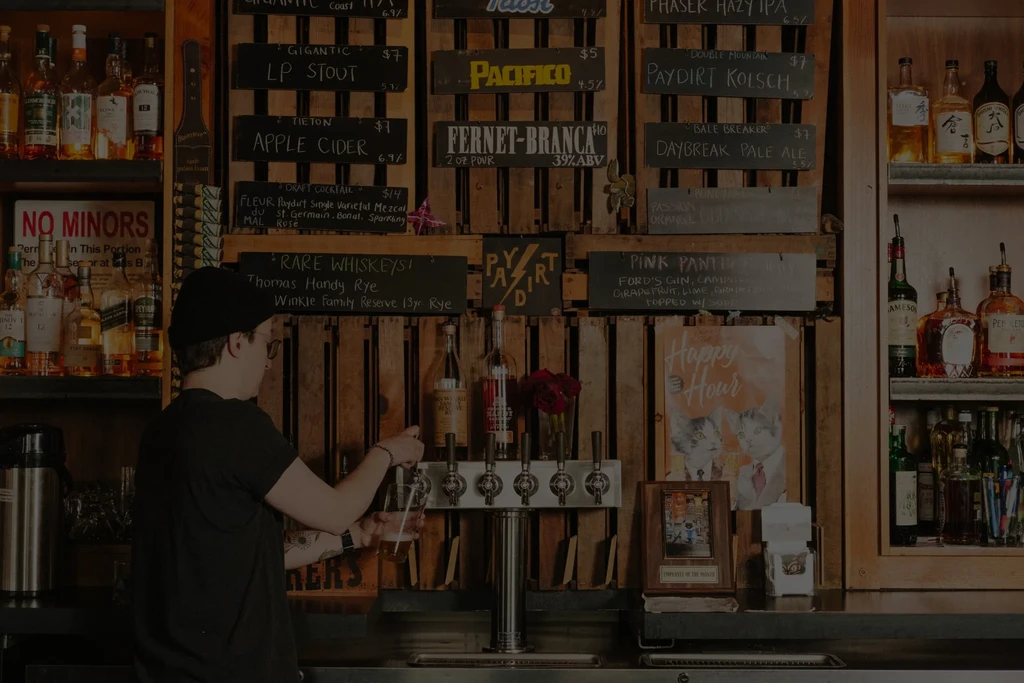 Bartender pouring a drink at a bar with detailed menus.