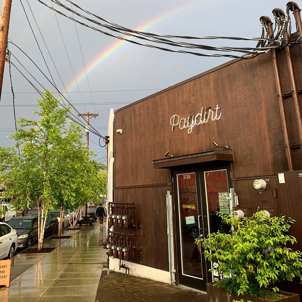 Paydirt building, neon sign, wet sidewalk, under an arched rainbow.