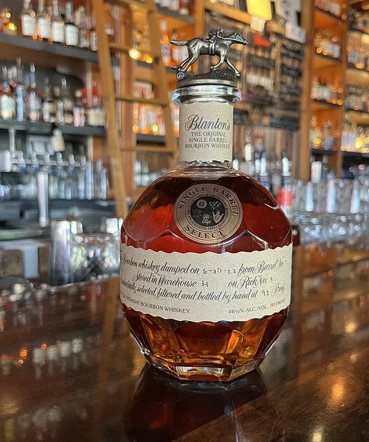 Blanton's bourbon bottle with jockey stopper on a wooden bar.