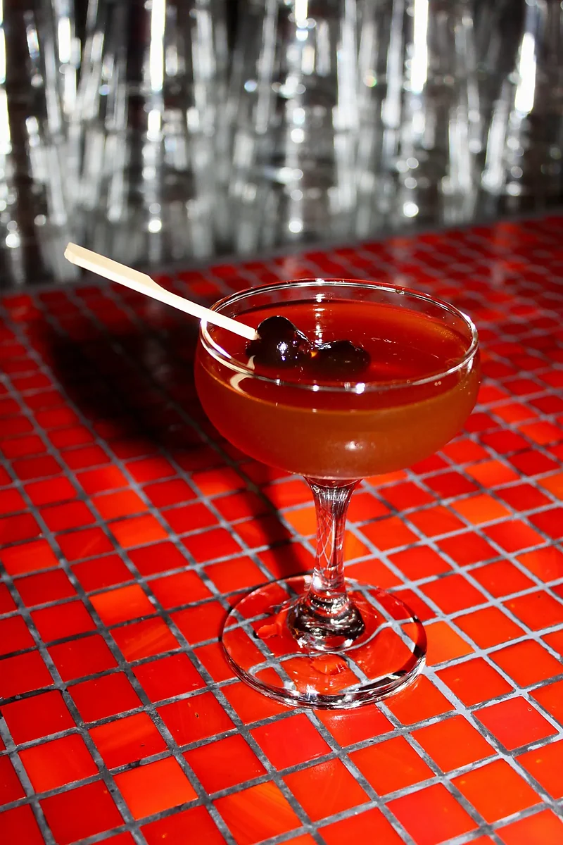 Manhattan cocktail in coupe glass with cherries on red tile