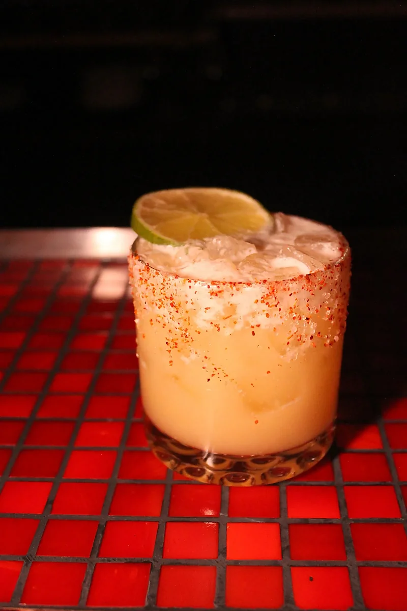 Chili-salt-rimmed margarita with lime wheel on red tile bar
