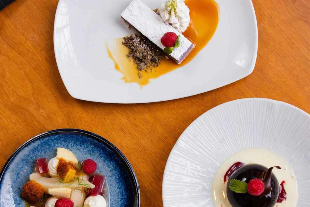 Three gourmet desserts elegantly plated on a wooden table.